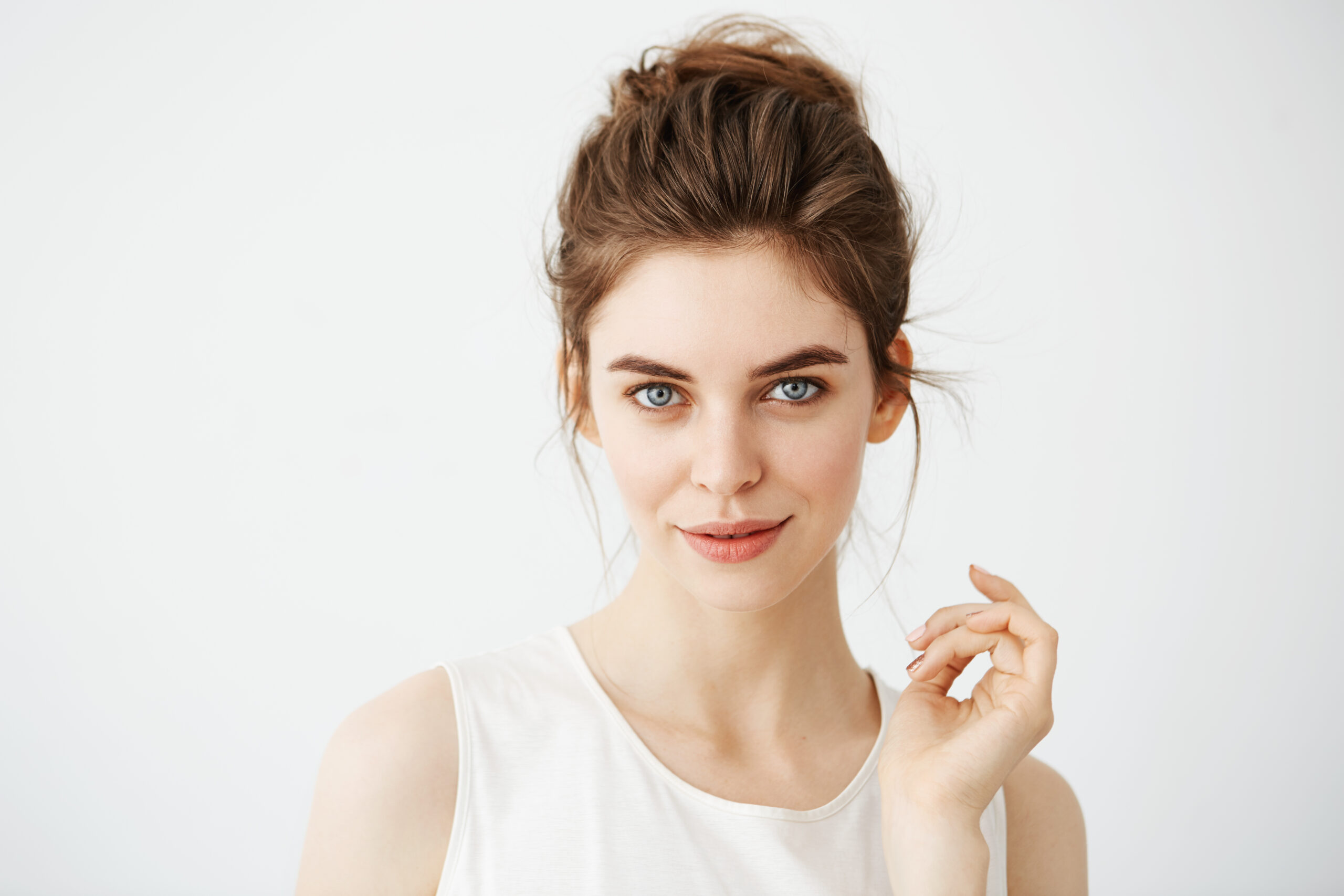 Portrait of young beautiful playful girl with bun looking at camera posing over white background. pigment