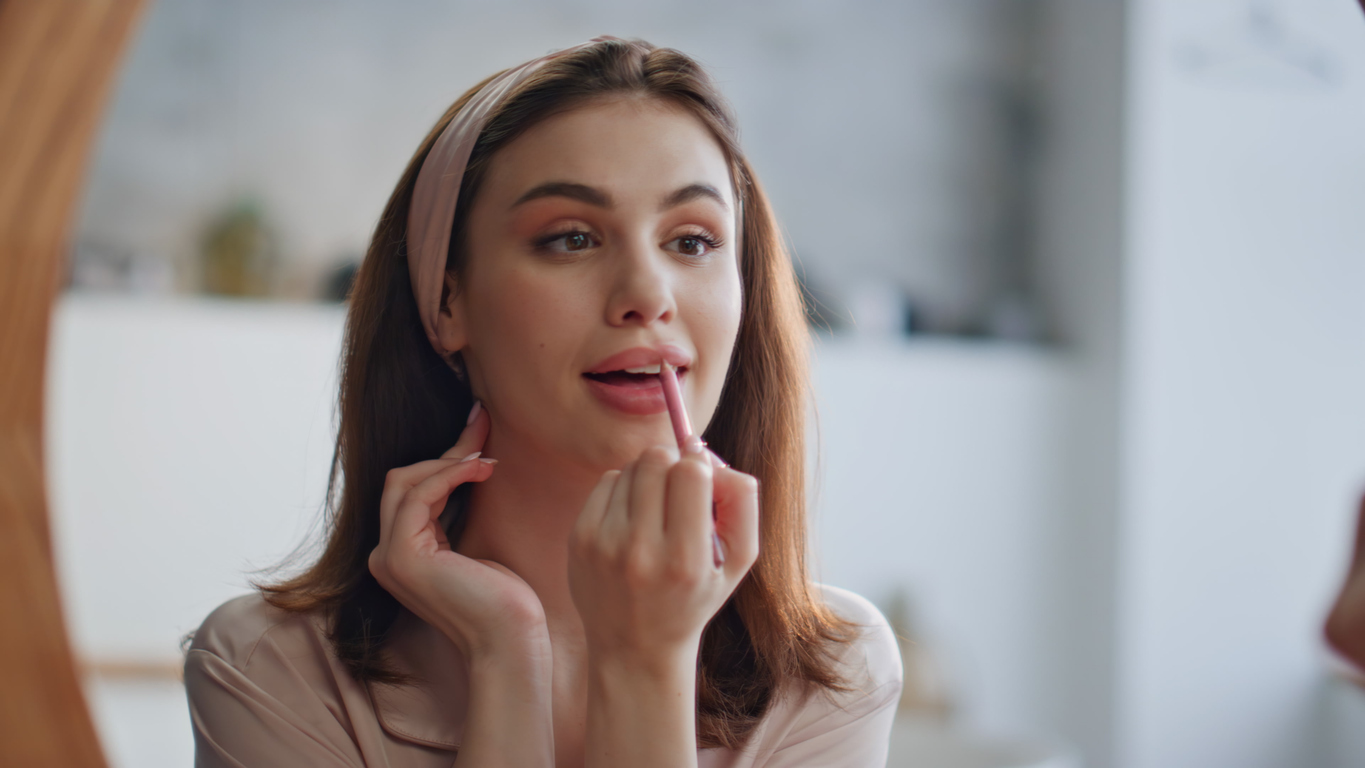 A woman stares in the mirror as she applies lip liner to her newly injected lips.